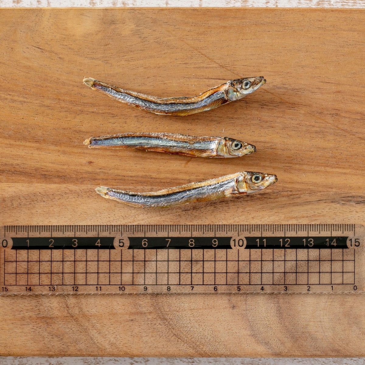 木製ボードの上に並べられた3匹の乾燥小魚と、サイズ確認用の定規